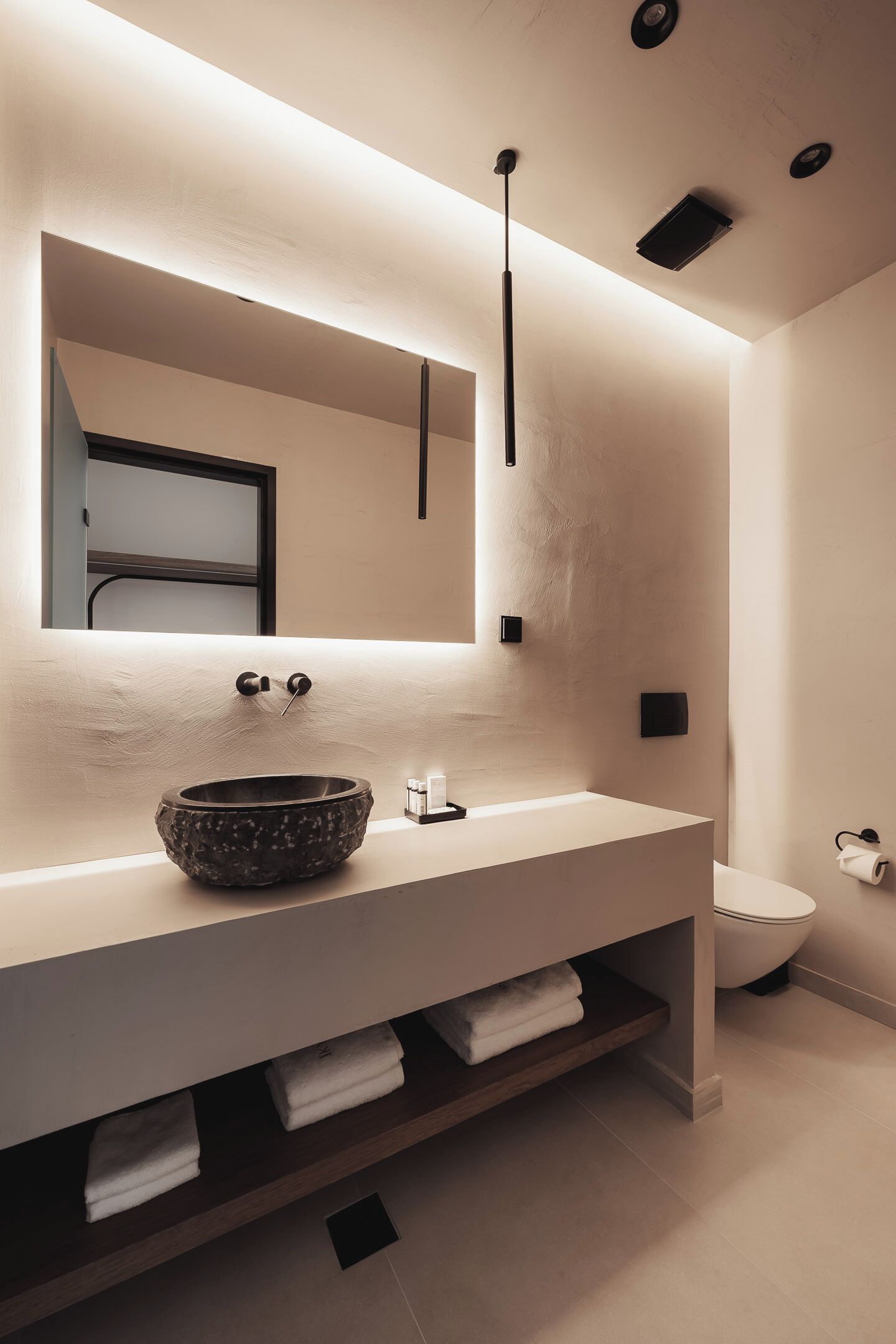 A modern bathroom with a large mirror, a stone basin sink, and a toilet.