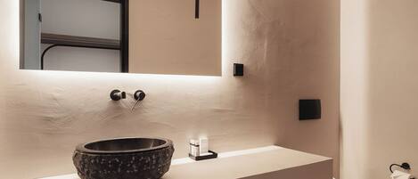 A modern bathroom with a large mirror, a stone basin sink, and a toilet.