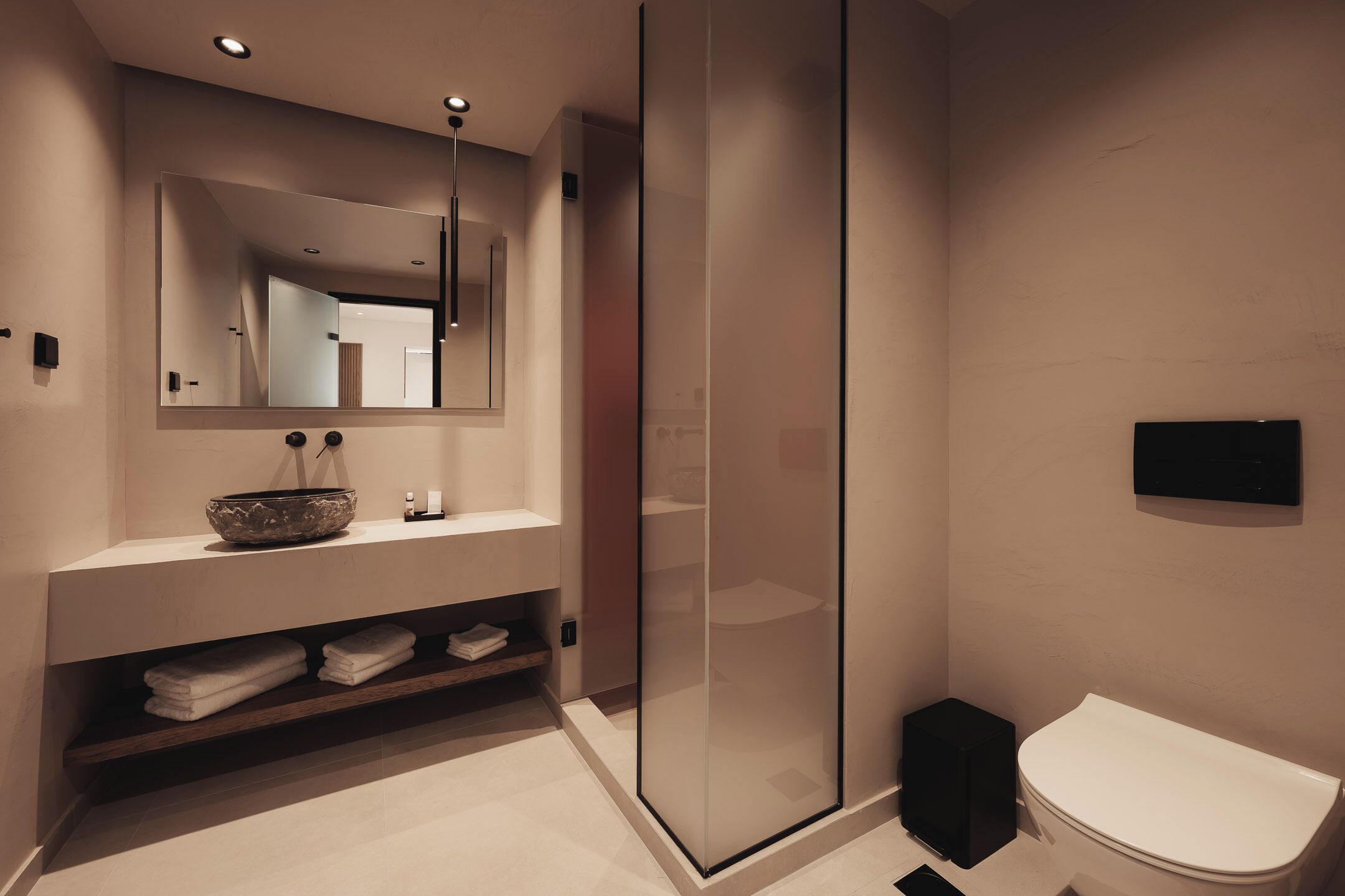 A modern bathroom with a glass shower enclosure, a white toilet, and a vanity with a bowl sink and mirror.