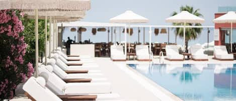 Zona junto a la piscina con tumbonas y sombrillas, cielo despejado y una piscina.