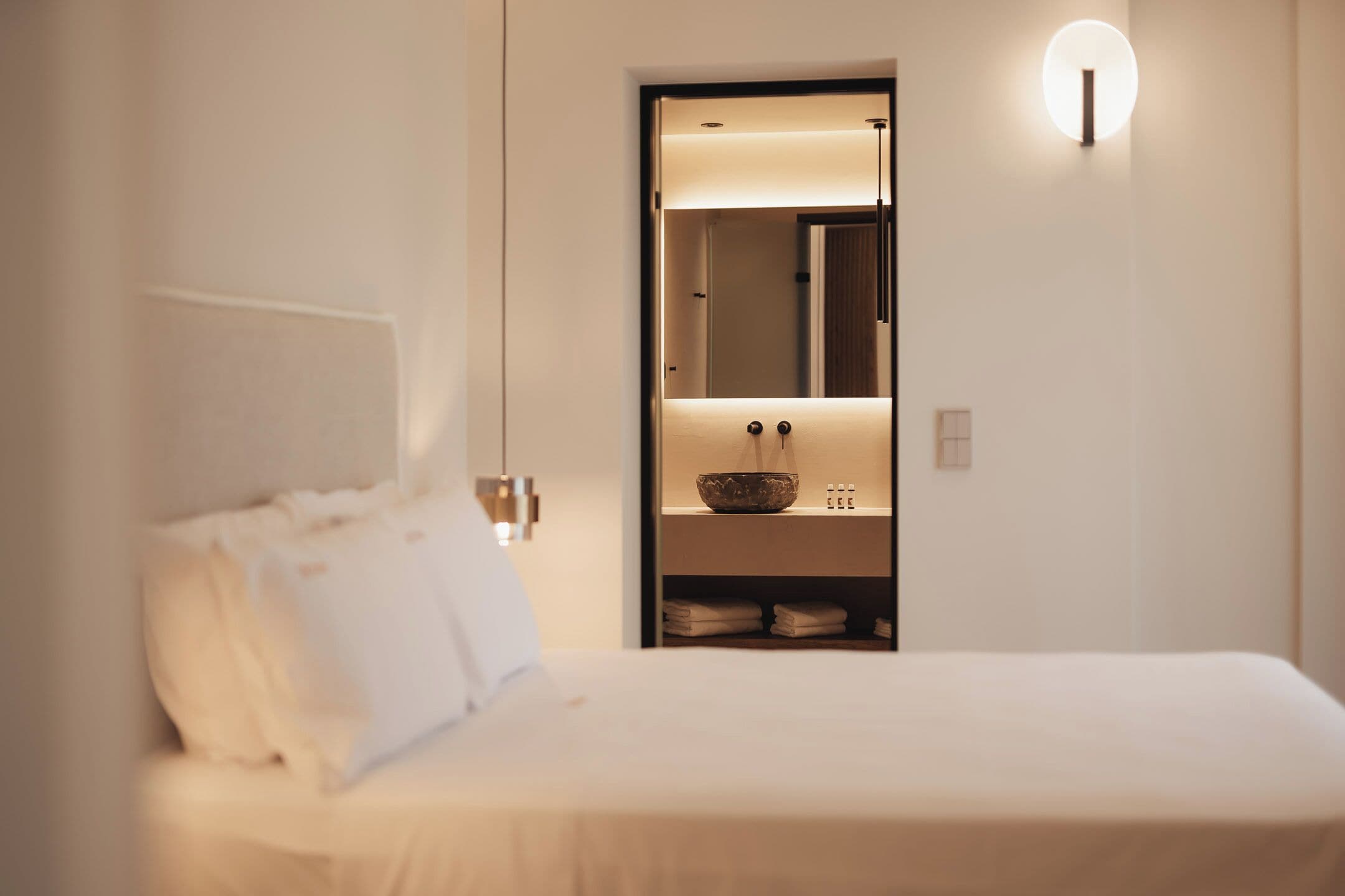 Una habitación de hotel moderna con una cama bien hecha, un armario empotrado con espejo y una lámpara de pared.
