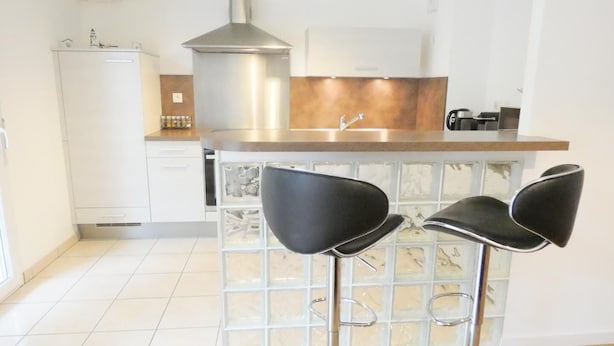 Eine moderne Küche mit einer Edelstahl-Dunstabzugshaube, einer Holz Arbeitsplatte und einem eingebauten Spülbecken. Es gibt drei schwarze Barhocker mit Metallbeinen.