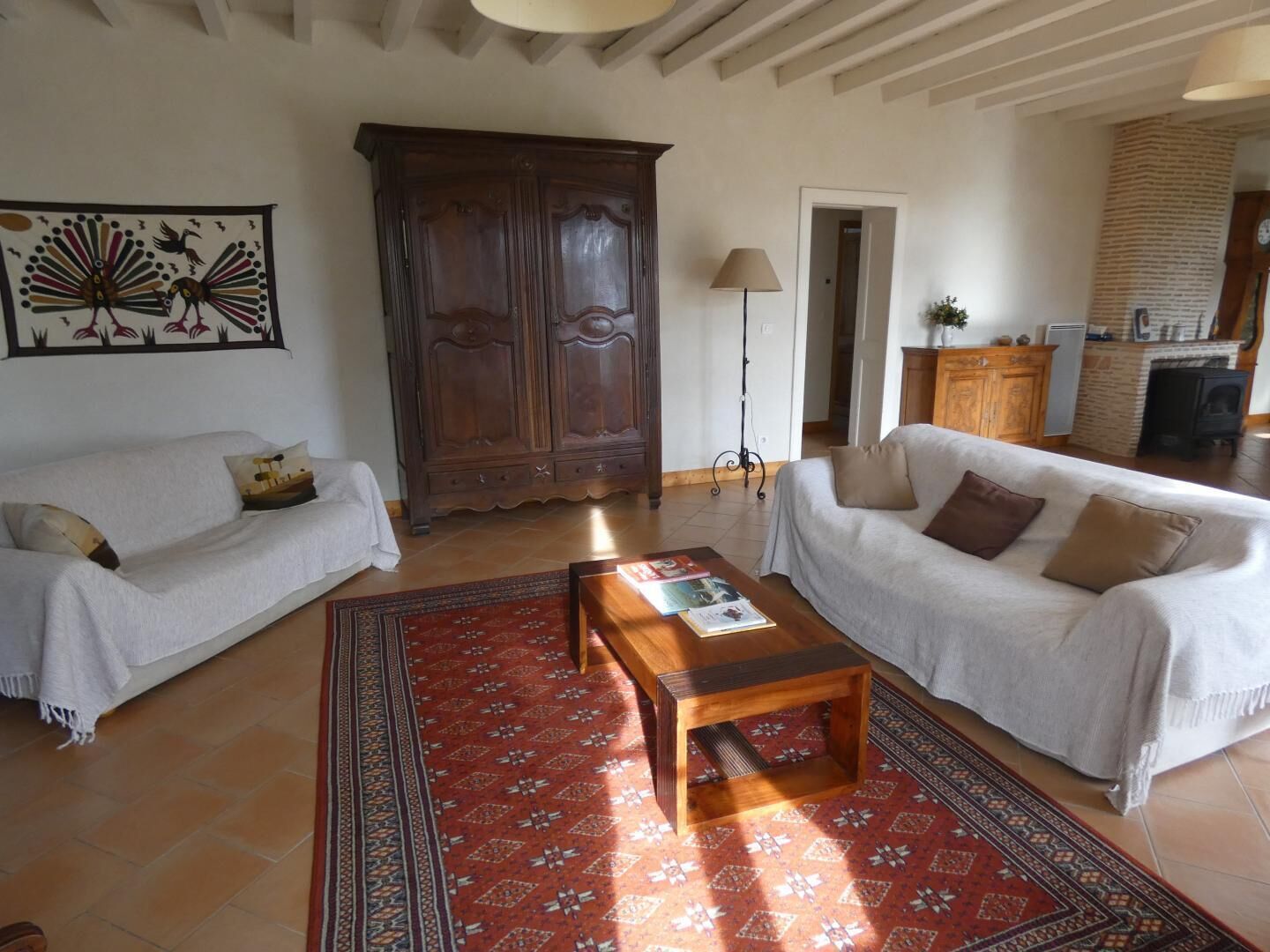 Sala de estar com dois sofás brancos, uma mesa de centro de madeira e um tapete estampado.