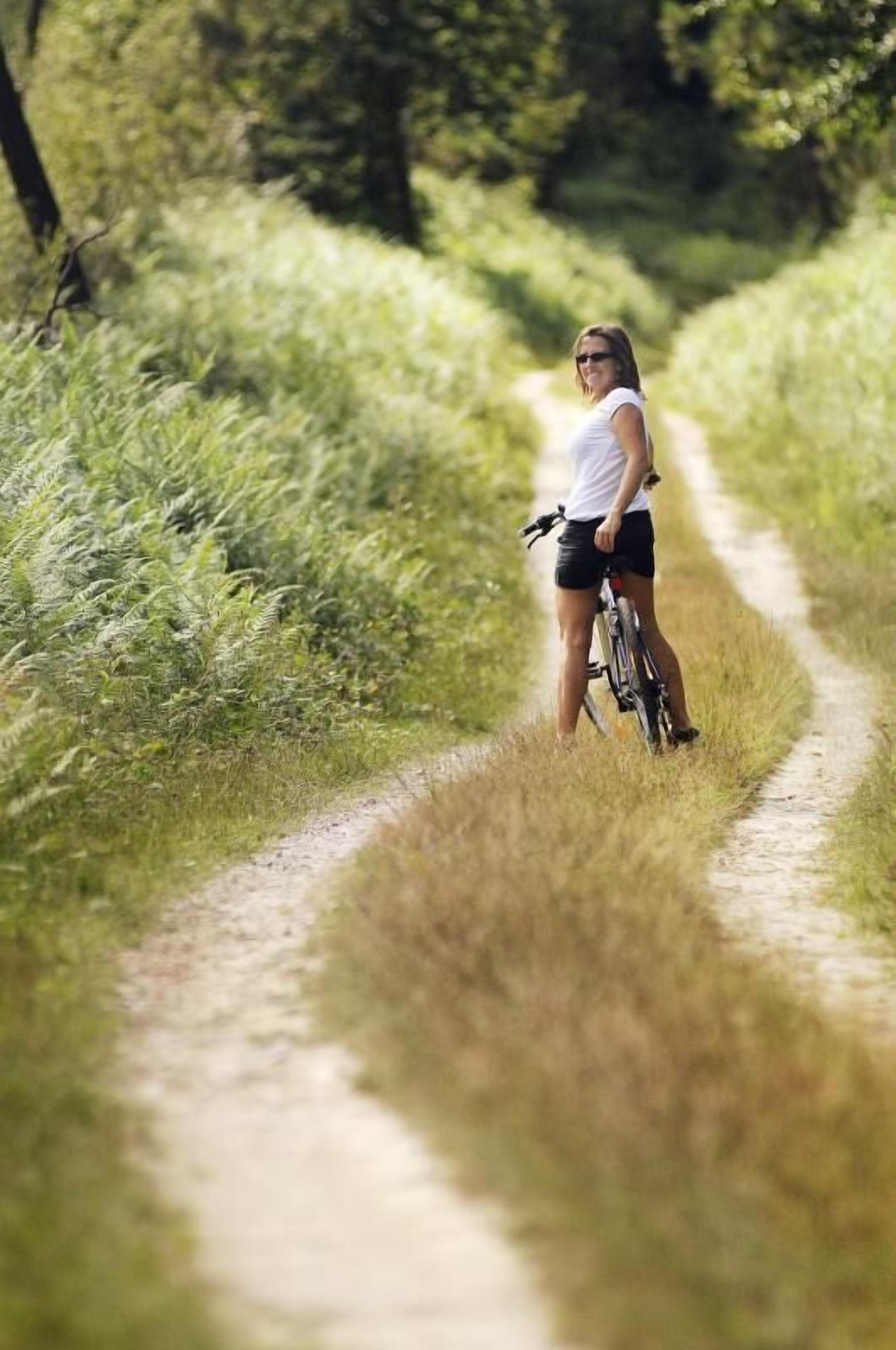 A person standing on a dirt path in a grassy area with trees in the background.