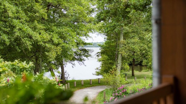A view of a lake from a wooden deck with a path leading to the water. - Côté Lac - Leon - Gîte (LEON)