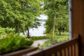 Blick auf einen See von einer Holzterrasse aus, ein Pfad führt zum Wasser.