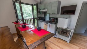 A kitchen with a wooden table, red placemats, a microwave, a stove, and a small oven. - Côté Lac - Leon - Gîte (LEON)