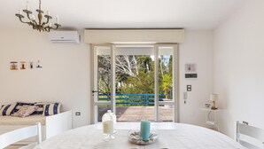 A room with a bed, a dining table with candles, a chandelier, and a view of a blue fence and trees outside. - 3335 Podere Li Noci by Barbarhouse (Melendugno)