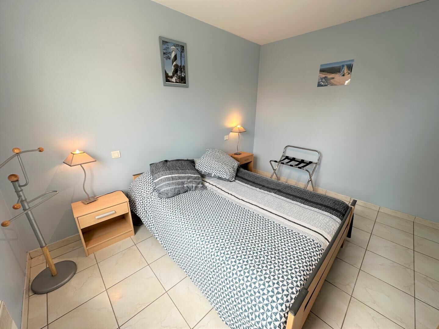 Une chambre à coucher comprenant un lit, deux tables de chevet, une lampe, une chaise et deux tableaux encadrés accrochés au mur.