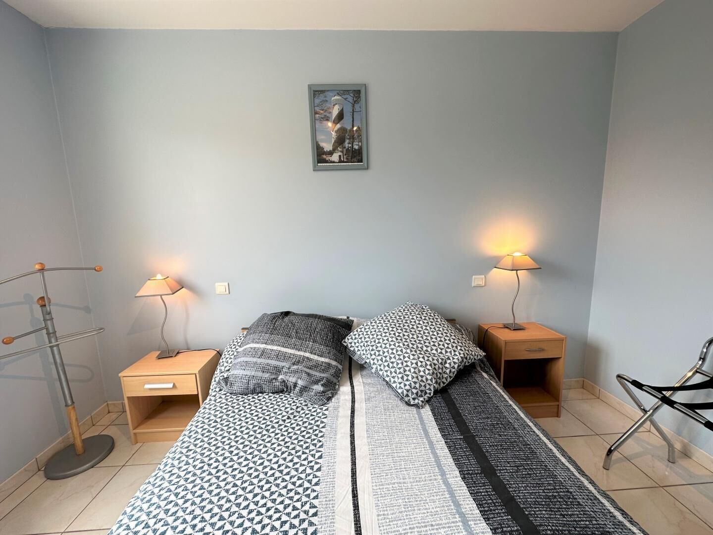 Un dormitorio pequeño y ordenado con dos camas, cada una con ropa de cama estampada y lámparas de noche.