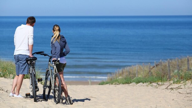 Dos personas en una playa arenosa con bicicletas, mirando al océano.