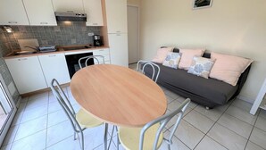 Un espacio habitable compacto con kitchenette, una mesa de comedor con sillas y un sofá con cojines decorativos.