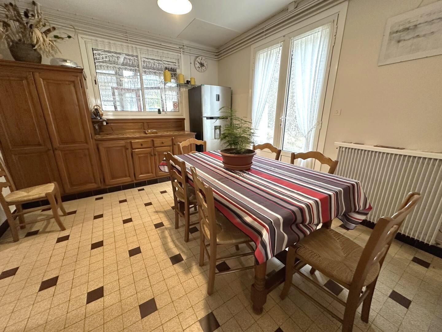 Eine Küche mit gefliestem Boden, Holzschränken, einem Tisch mit gestreifter Tischdecke und Stühlen.