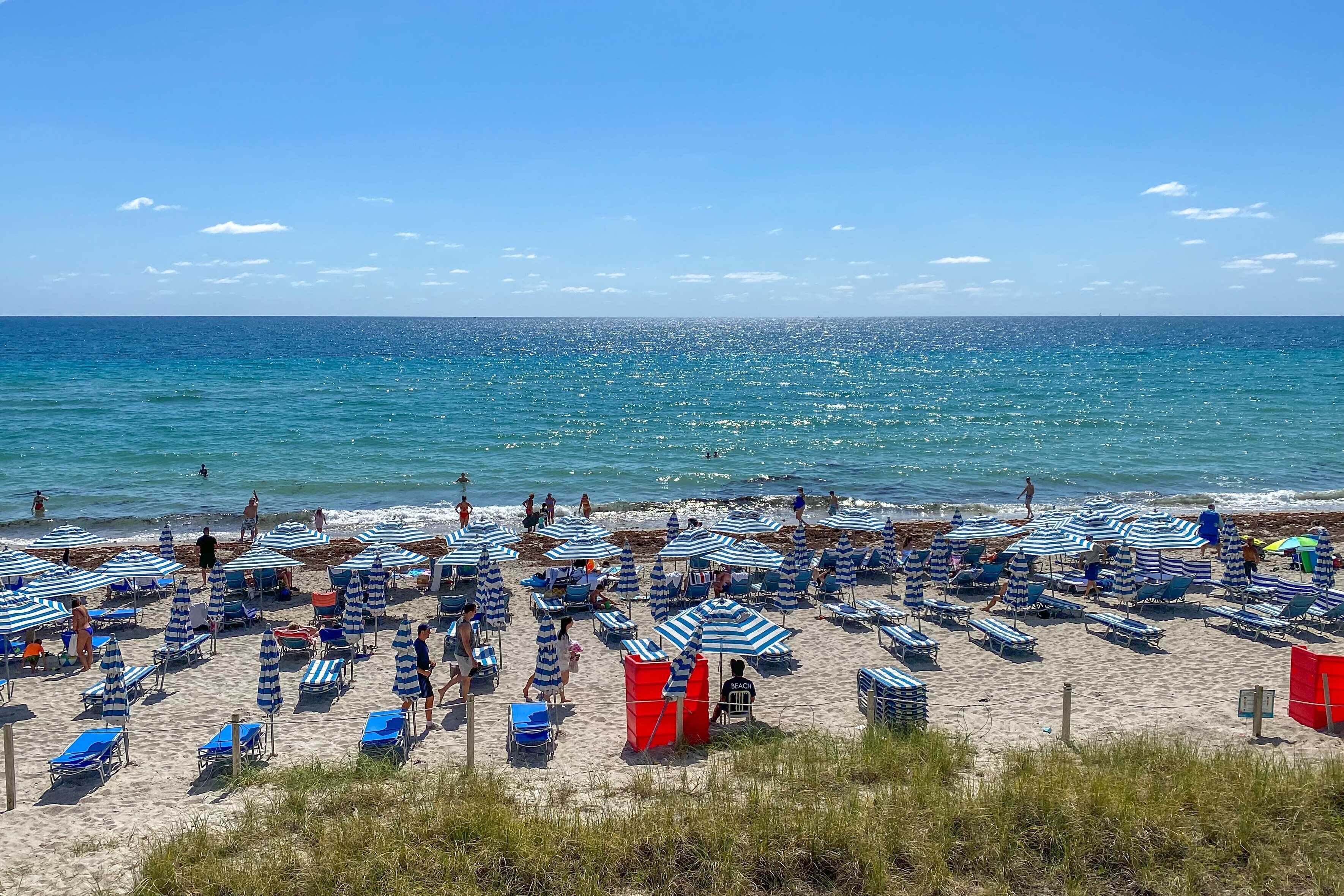 Ein Strand mit blauen und weißen Streifen, gesäumt von Liegestühlen und Sonnenschirmen.