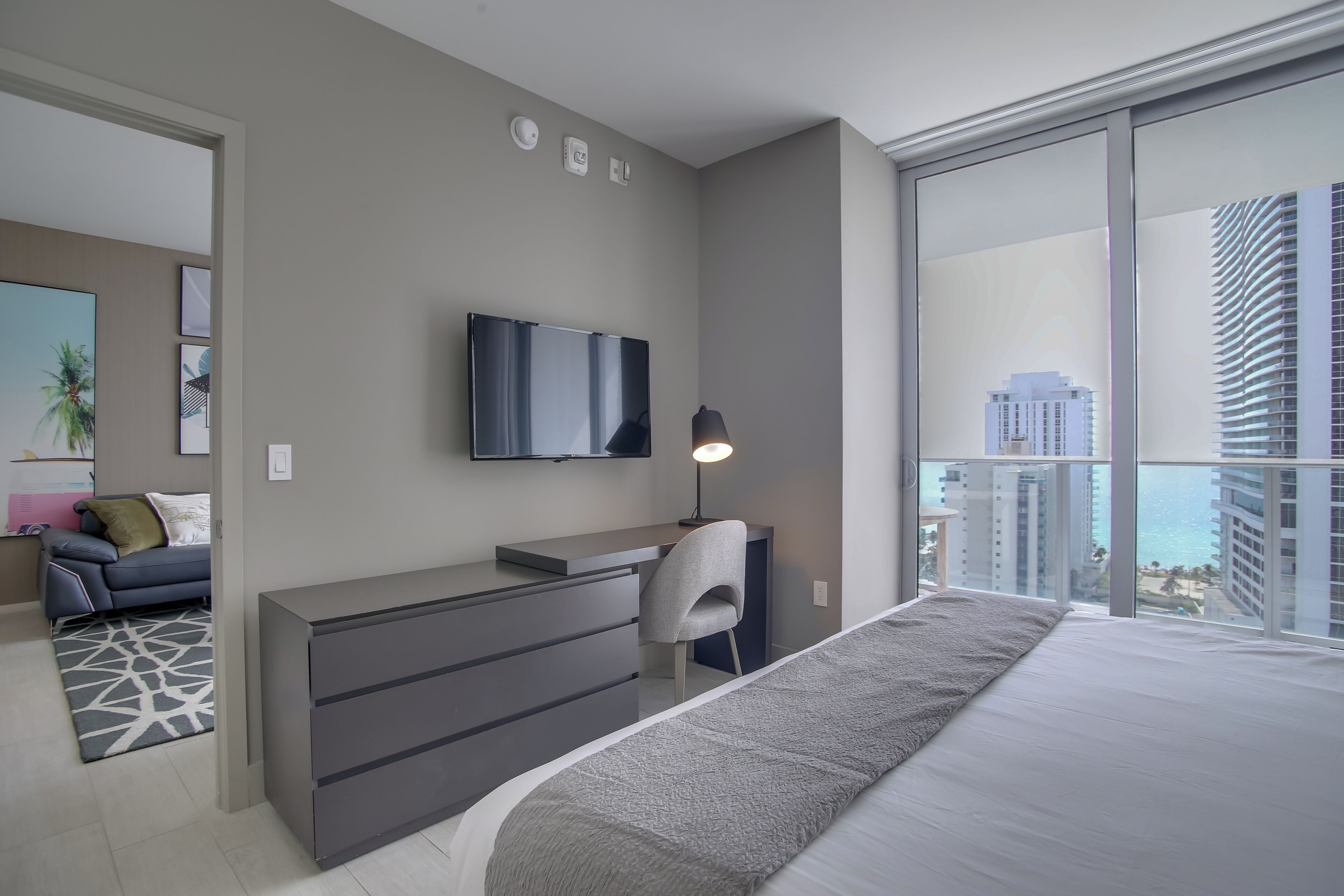 Une chambre d’hôtel moderne dotée d’un grand lit, d’un bureau avec une chaise, d’une télévision à écran plat et d’un balcon offrant une vue sur la ville.