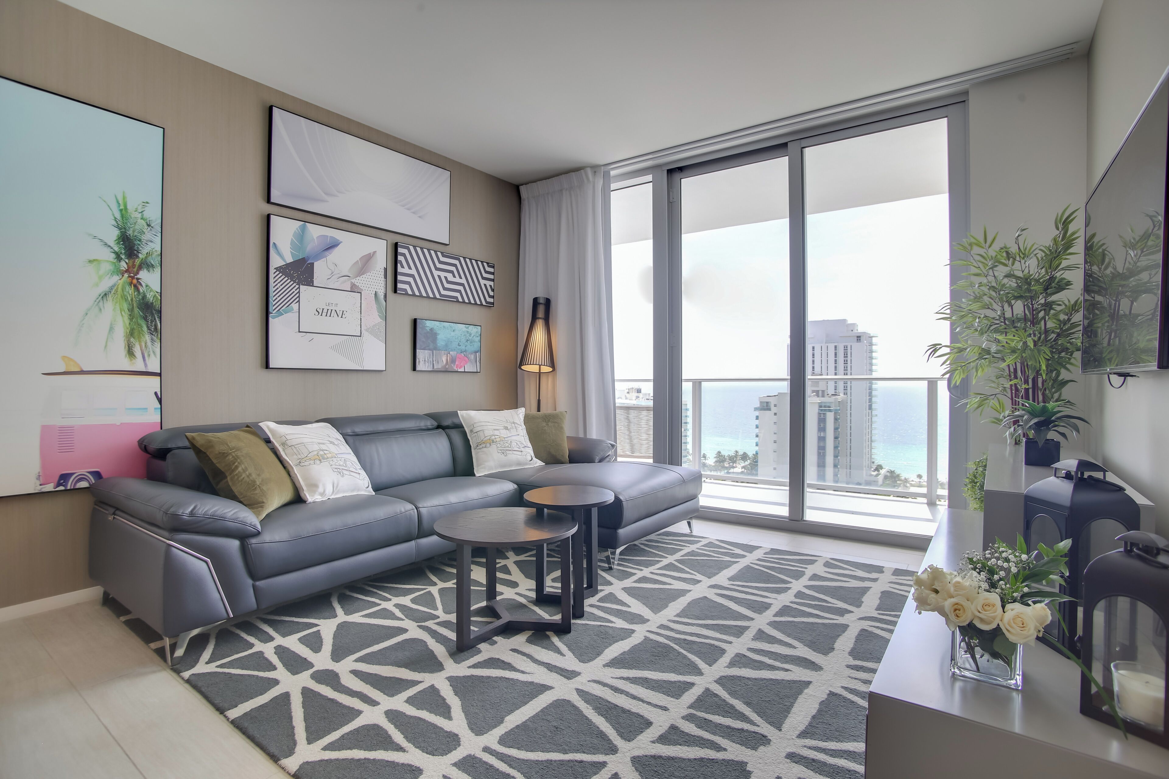 A modern living room with a grey sofa, two side tables, and a large window with a view of the city.