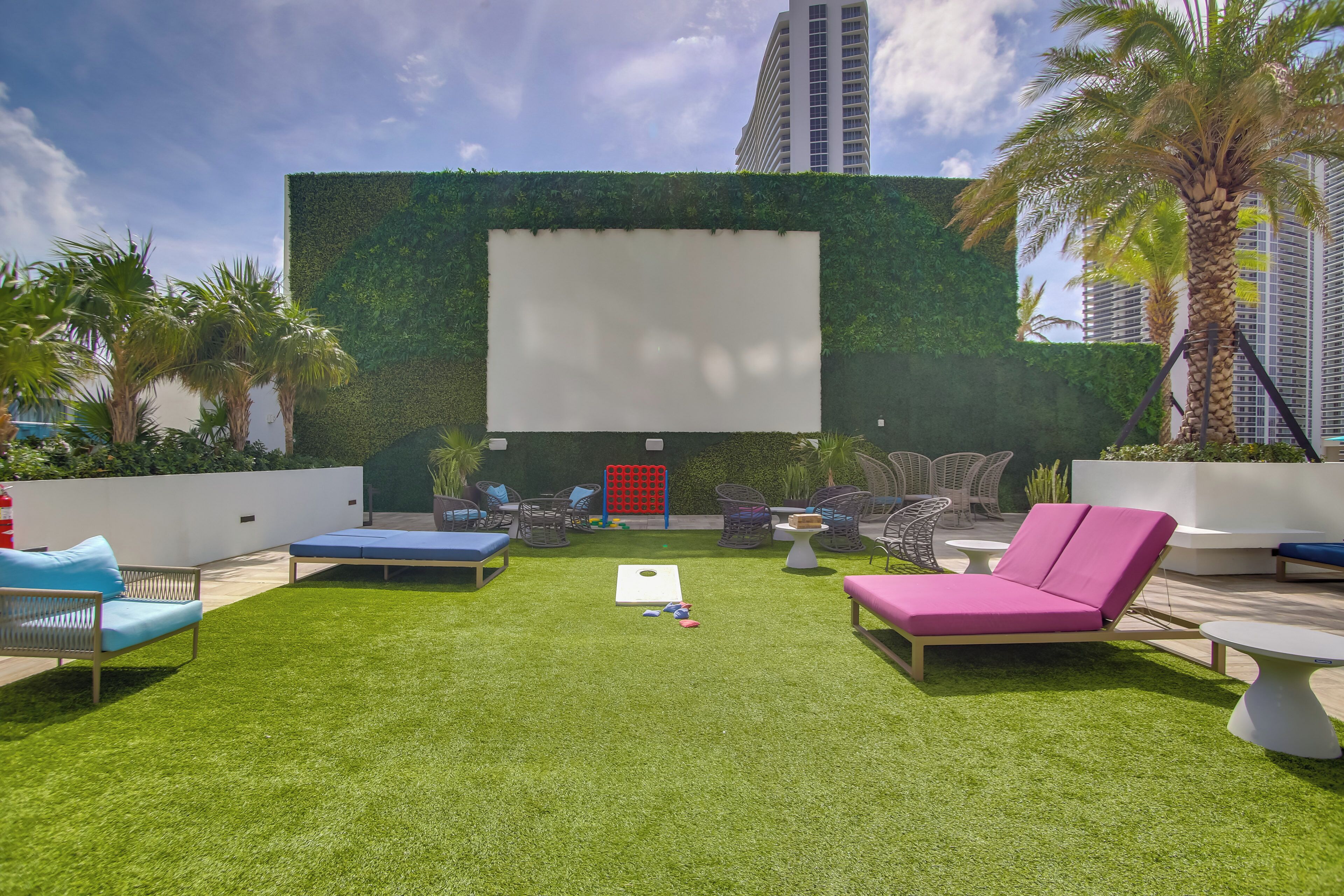 A rooftop lounge with a green wall, outdoor seating, and a blank screen.
