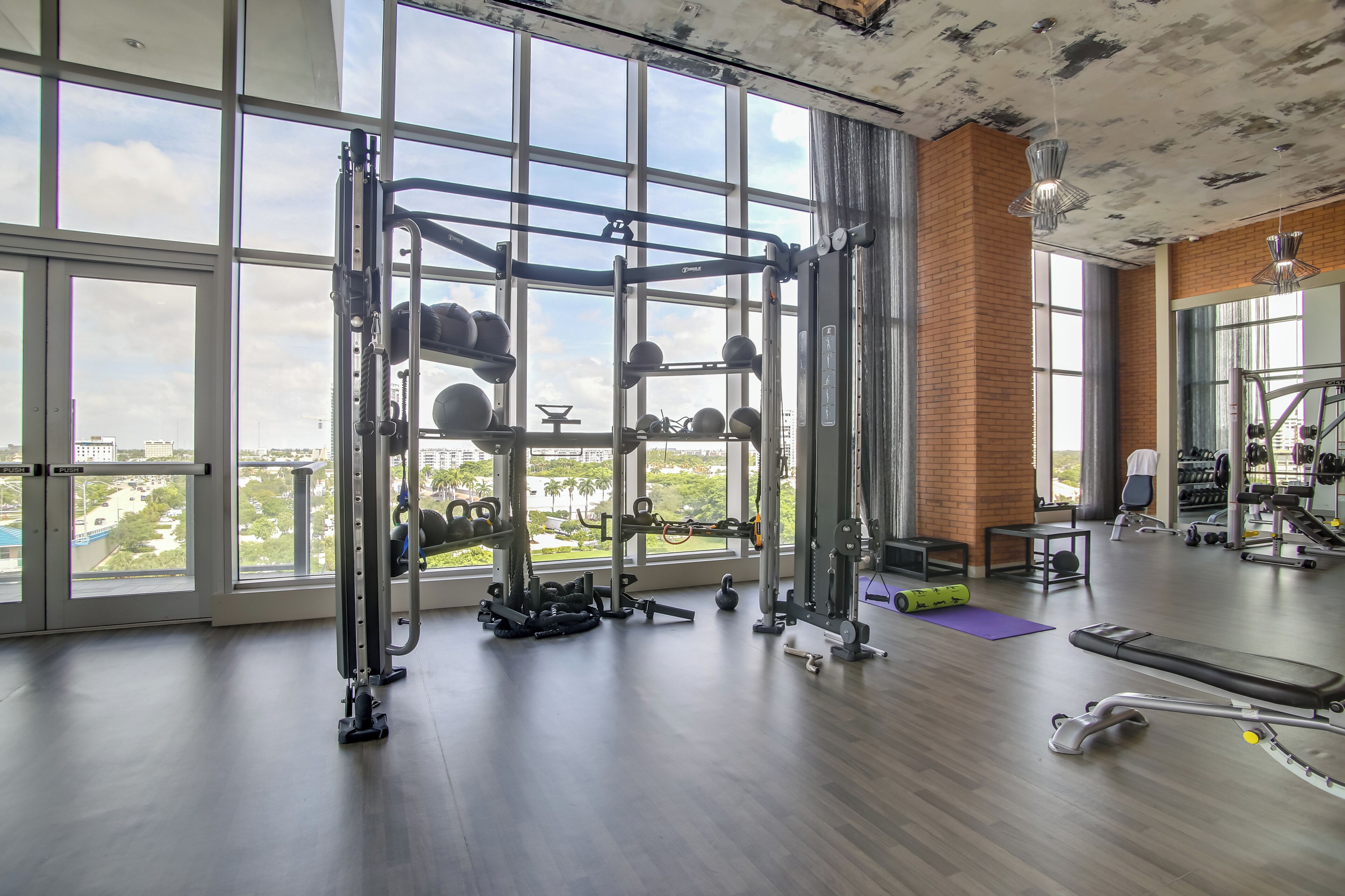 A gym with large windows, weightlifting equipment, and a view of the city.