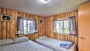 Ein Zimmer mit Holzwänden, zwei Betten mit gemusterten Bettdecken und Vorhängen an den Fenstern.