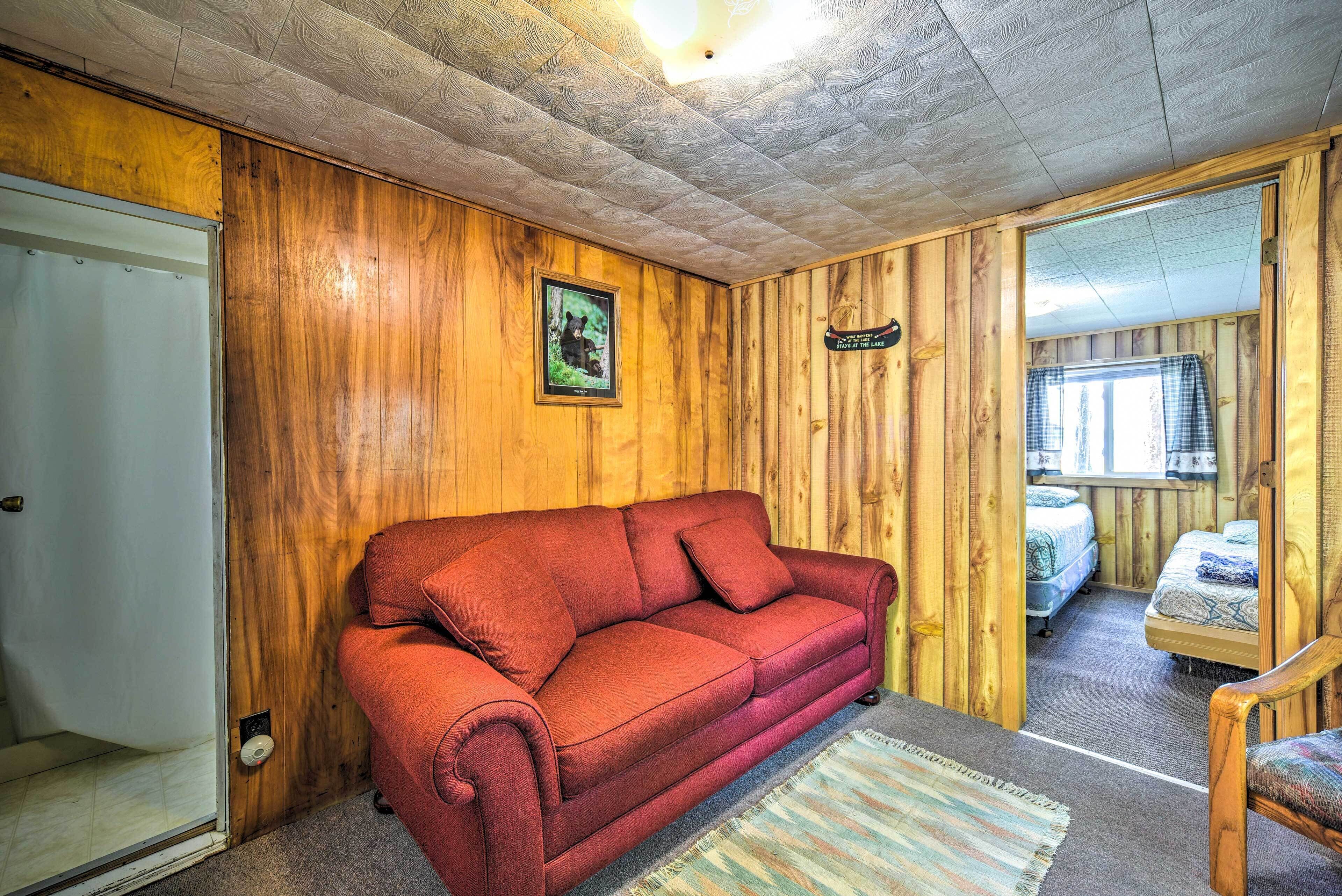 Ein gemütliches Zimmer mit einem roten Sofa, einer Holzwand, einem gerahmten Bild und einem Bett mit einem karierten Vorhang.