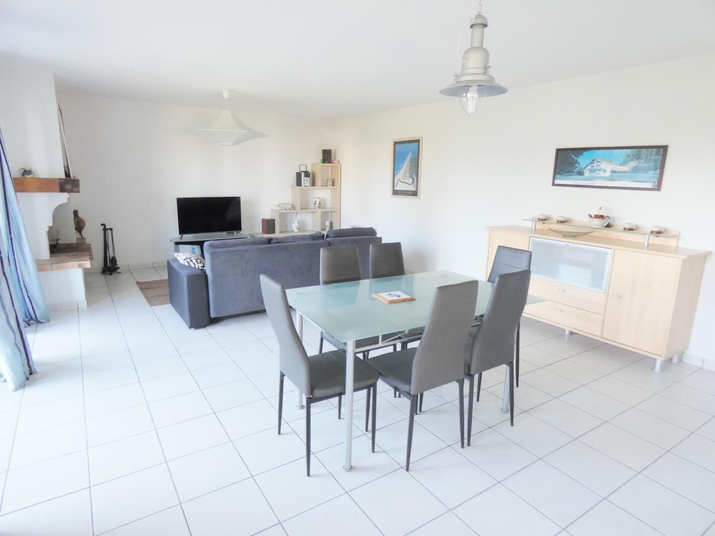 A modern living room with a grey sofa, a glass dining table, and a TV.