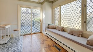 Ein Zimmer mit Holzboden, einer weißen Bank mit Kissen, einem weißen Schrank und einem gemusterten Teppich.