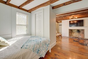 A bedroom with a bed, a white door, a window with blinds, a fireplace, and a dining area with a table and chairs. - Near Route 6A & Village Shops! East Sandwich Haven (East Sandwich)