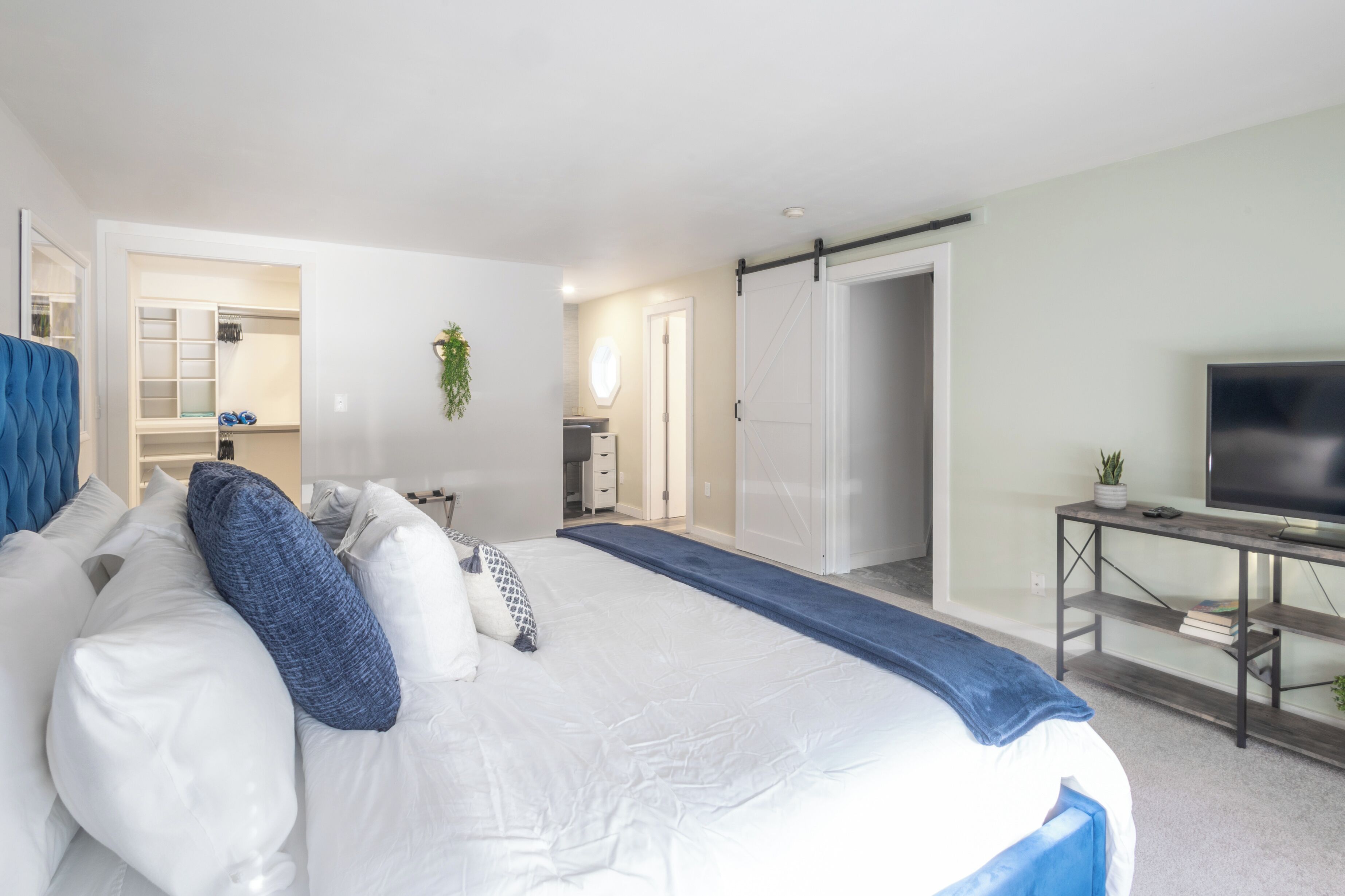Een slaapkamer met een groot bed, een televisie op een houten standaard en een inloopkast met schuifdeuren.