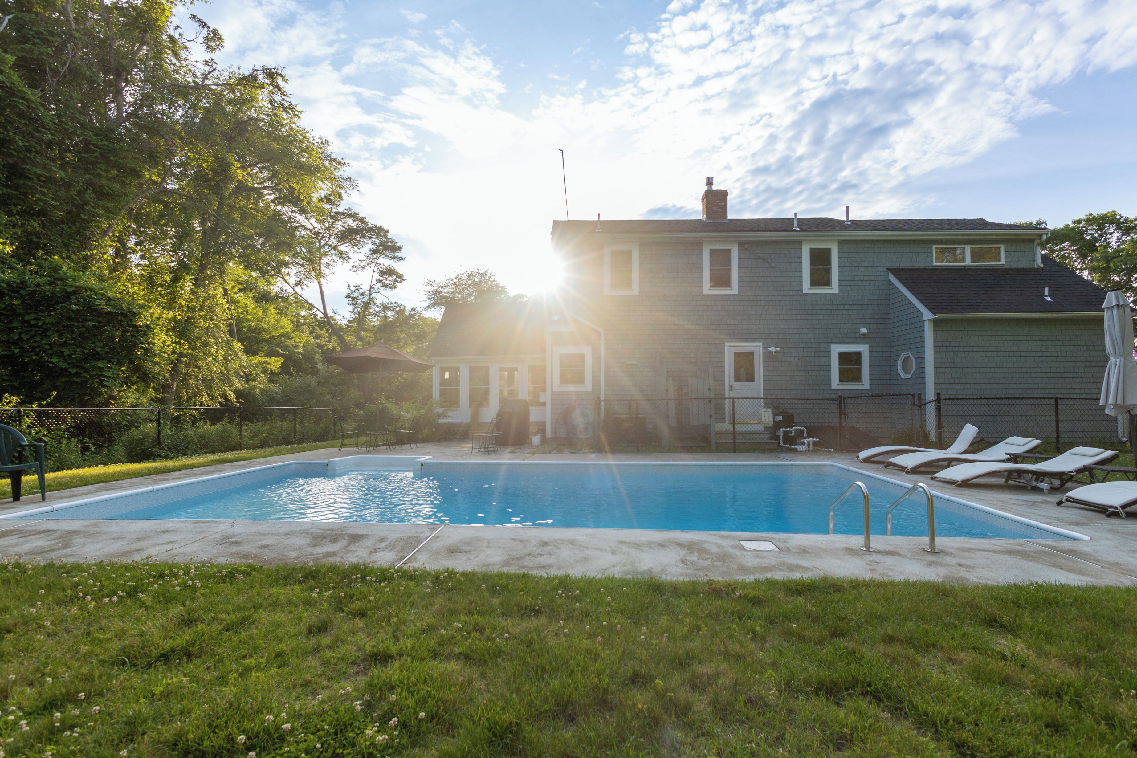 Una piscina con lettini, una casa sullo sfondo e un cielo sereno.