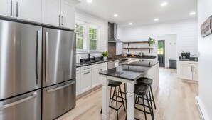 A modern kitchen with stainless steel appliances, white cabinetry, and a central island with bar stools. - 8 bedroom Manor - Hot Tub - Game Room - Fire Pit - Sleeps 22 (Mount Pocono)
