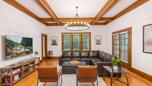 A living room with a large flat-screen TV, leather sofas, a glass coffee table, and wooden flooring. - 8 bedroom Manor - Hot Tub - Game Room - Fire Pit - Sleeps 22 (Mount Pocono)