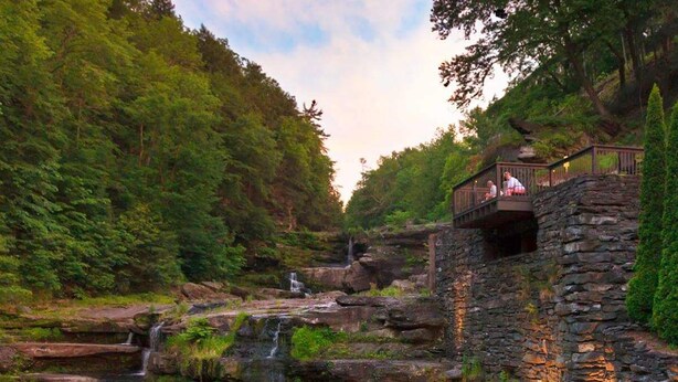 A stone bridge with a wooden deck, overlooking a cascading waterfall and lush greenery. - 8 bedroom Manor - Hot Tub - Game Room - Fire Pit - Sleeps 22 (Mount Pocono)