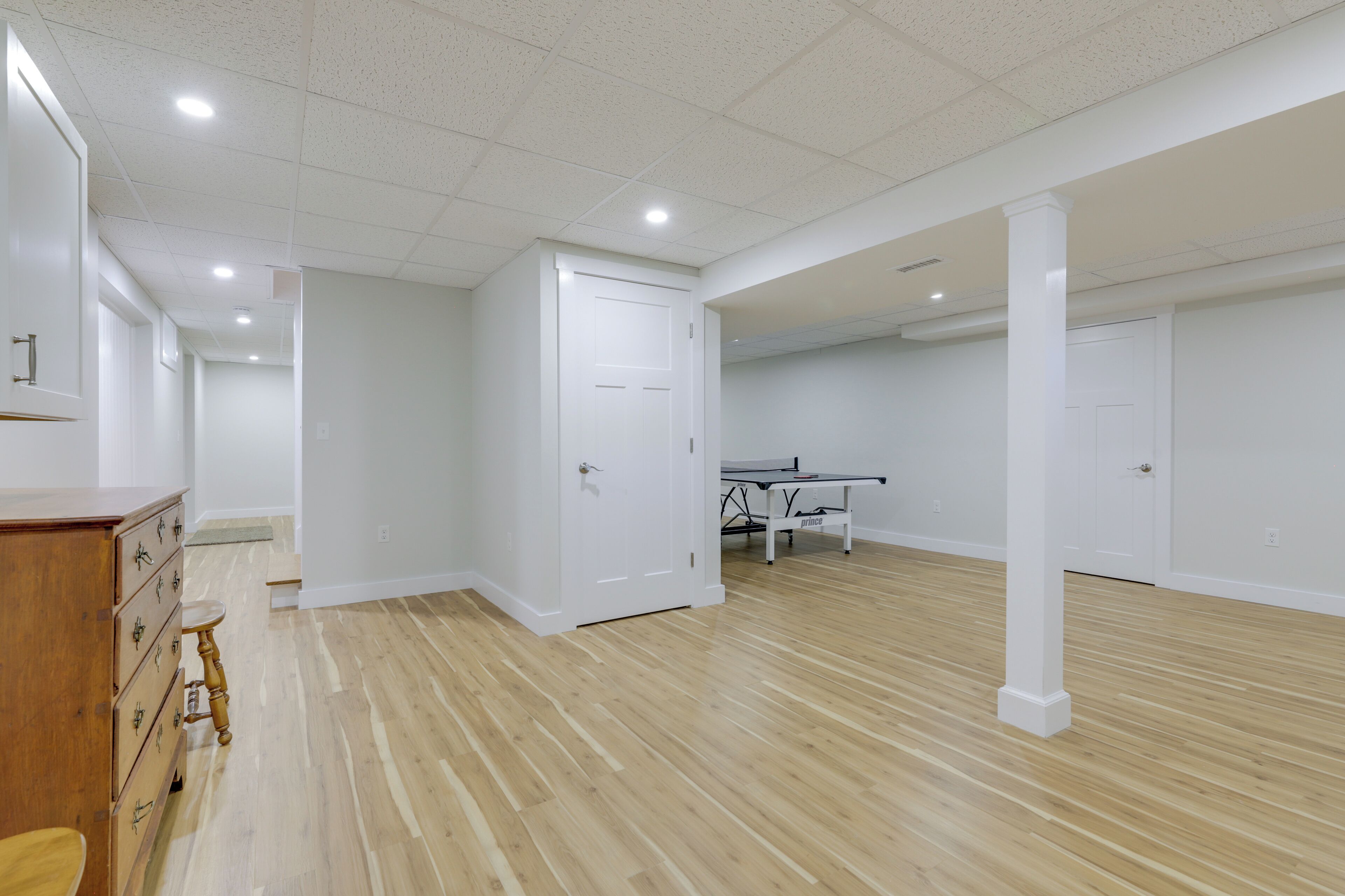 Una habitación amplia con piso de madera, paredes blancas y una mesa de ping pong.