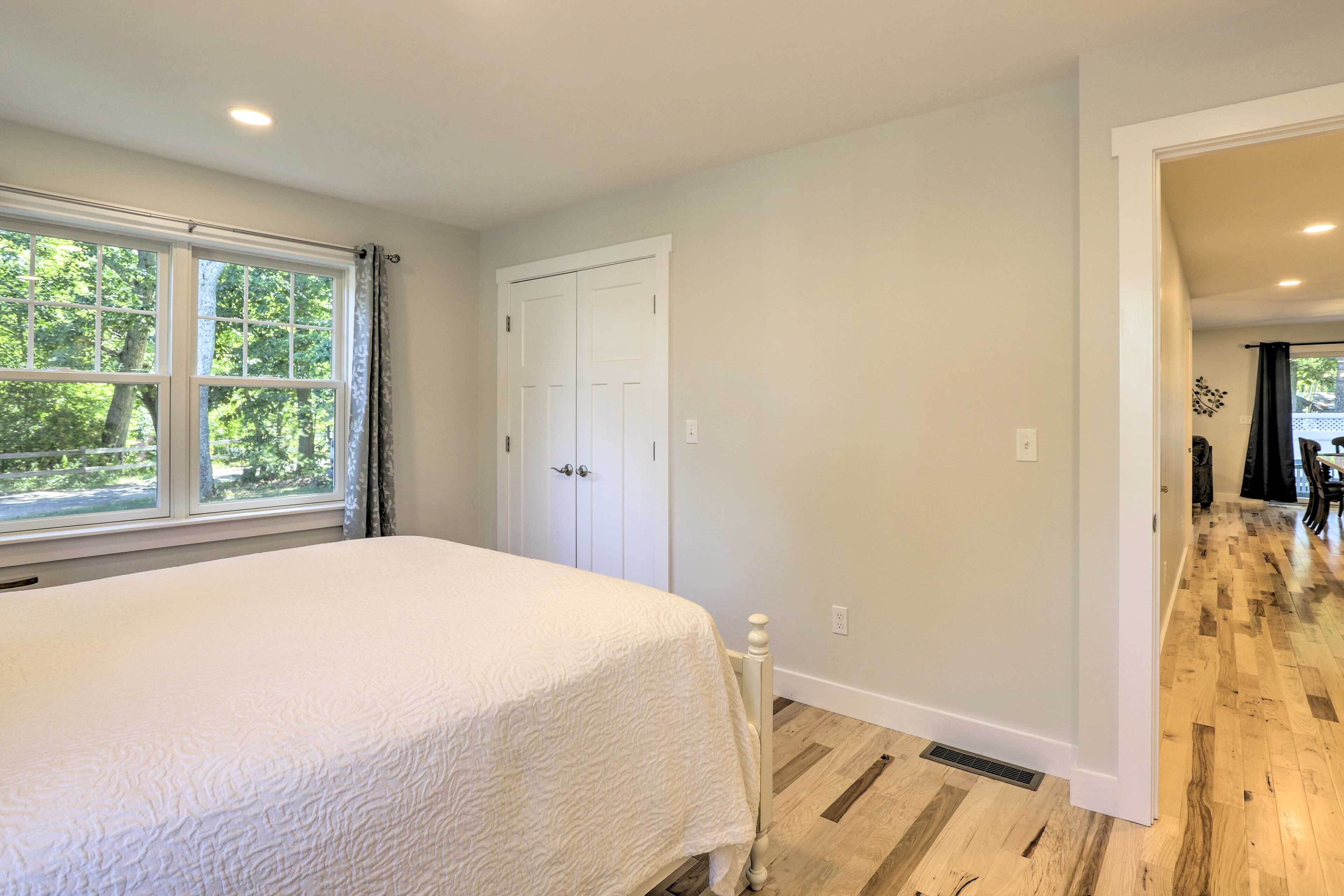 A bedroom with a large bed, a white door, and a view of a wooden floor and a window with curtains.