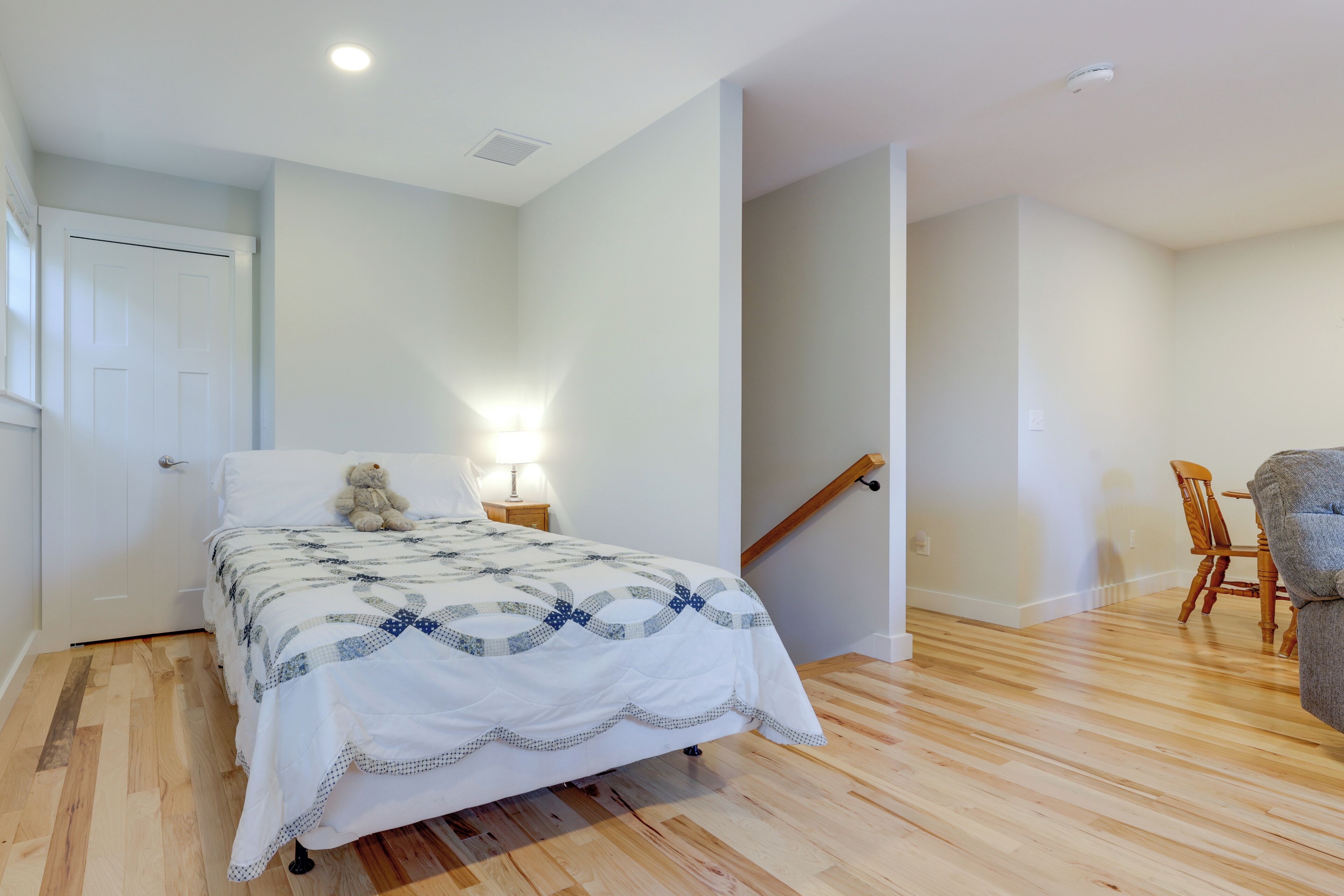 A bedroom with a bed, a nightstand, a teddy bear, a lamp, and a staircase leading to another room.