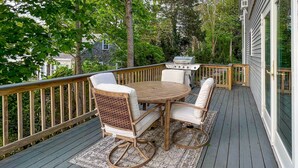 Eine Holzterrasse mit Tisch, Stühlen, einem Grill und Blick auf ein Haus.