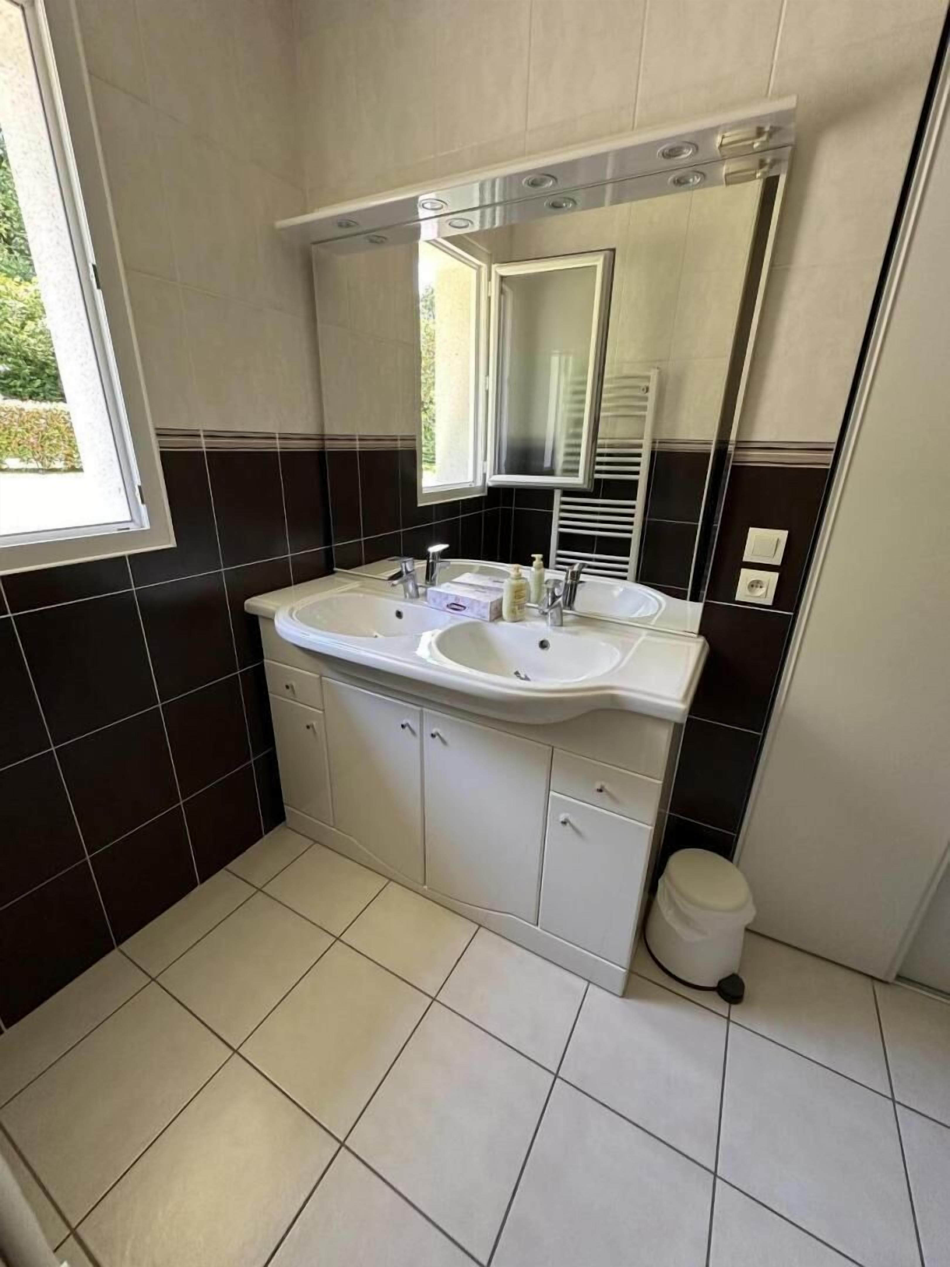 Un baño con un lavabo blanco, dos armarios, un espejo y una ventana.