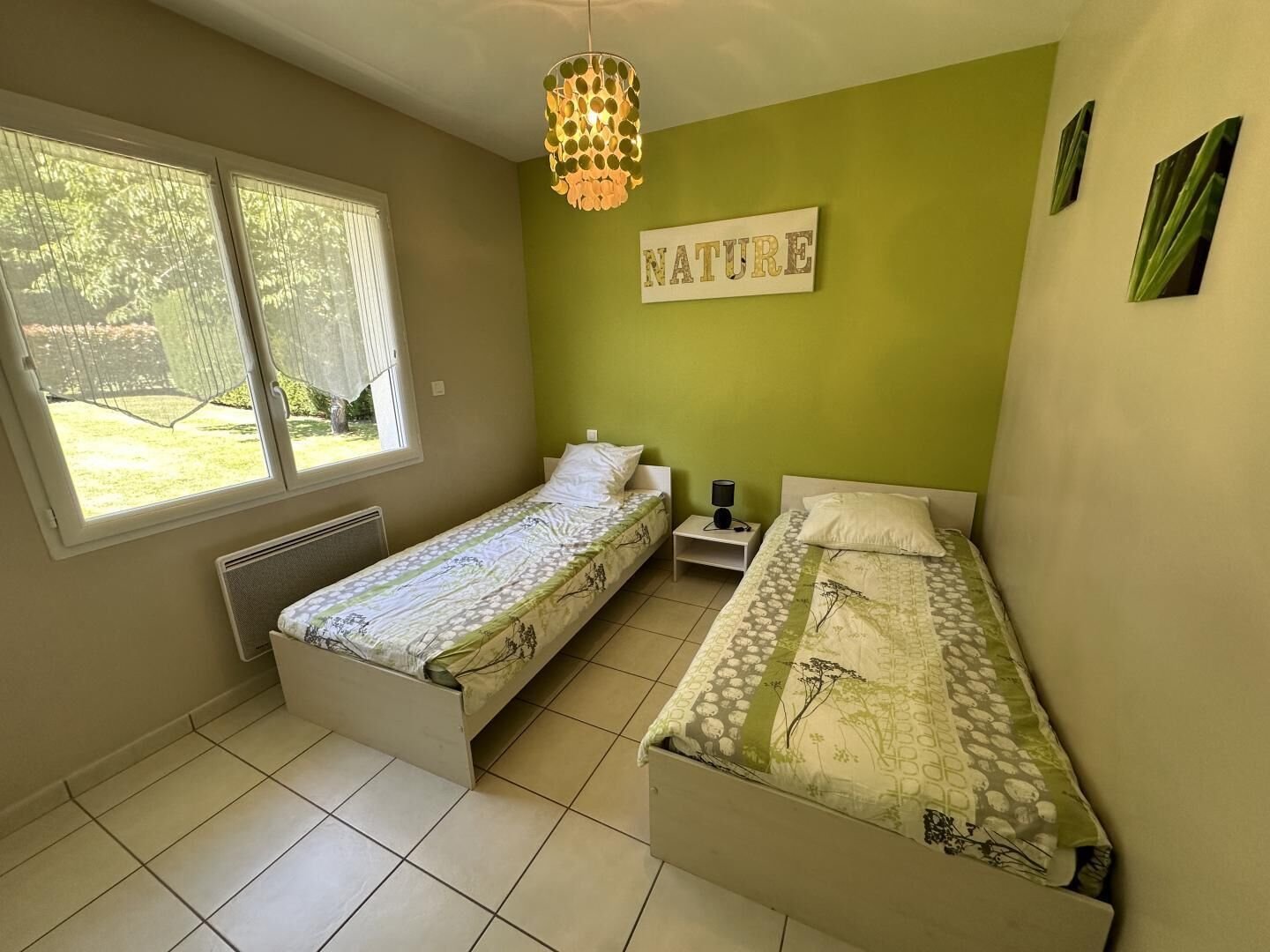 Un dormitorio con dos camas individuales, una ventana con cortinas, un cartel en la pared que dice "NATURE" y una lámpara colgante.