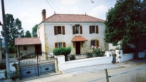A two-story house with a tiled roof, a front gate, and a small garden with flowers.