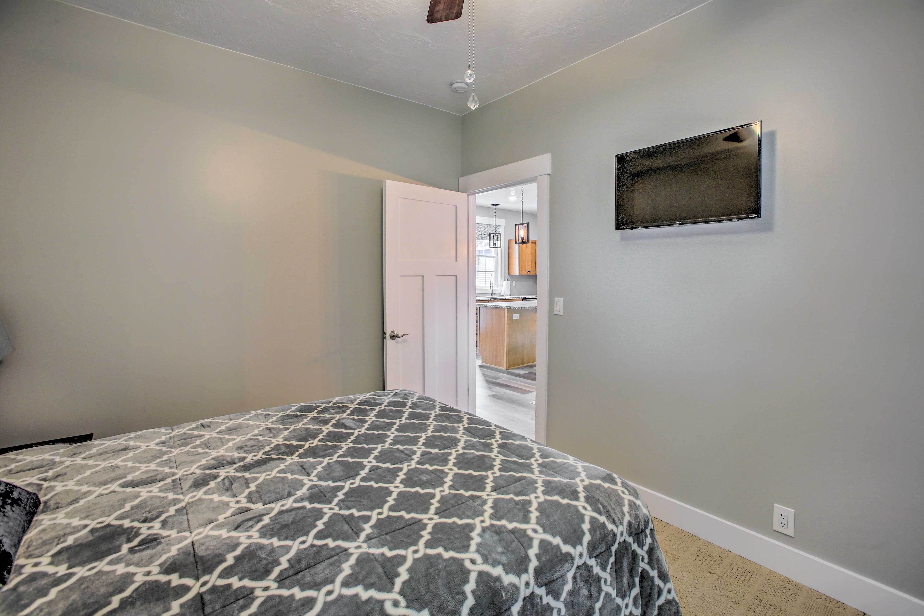 A bedroom with a patterned bedspread, a white door leading to a hallway, and a mounted TV on the wall.