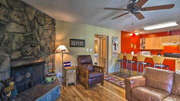 A living room with a stone fireplace, leather sofa, and a kitchen area with red walls and bar stools.
