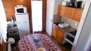 A compact kitchen with a microwave, coffee maker, and a small refrigerator. There's a dining table with a patterned tablecloth and a basket. - La Bardane - Brocas - Gîte (BROCAS)