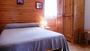 A bedroom with a wooden wall, a bed, a nightstand with a lamp, and a wardrobe. - La Bardane - Brocas - Gîte (BROCAS)