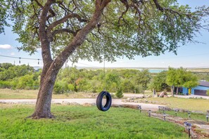 A tree with a tire swing hanging from its branches, a grassy area, and a building in the background.