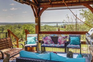 A covered outdoor seating area with wicker furniture and cushions, overlooking a scenic landscape with a body of water and hills. - Pet-friendly Canyon Lake Cabin, 1 Mi to Water! (Canyon Lake)