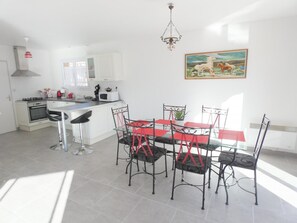 A modern kitchen with white cabinets, a gas stove, and a microwave. There is a dining area with a red table and black chairs. A chandelier hangs from the ceiling, and a painting of horses is on the wall.
