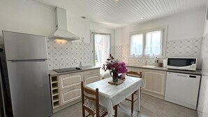Une cuisine moderne avec des meubles blancs, un réfrigérateur en acier inoxydable, un four à micro-ondes et une table à manger avec des chaises.