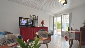 Un salon moderne comprenant une télévision, un meuble rouge, deux fauteuils à motifs, une table à manger avec des chaises et un vase rempli de fleurs.