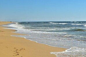 A beach with waves gently lapping onto the shore, a clear sky, and a few people in the distance. - Plein Vent - Soustons (SOUSTONS)