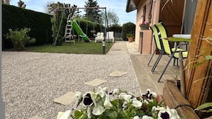 Un espace patio comprenant une aire de jeux pour enfants, des sièges d’extérieur et un parterre de fleurs.